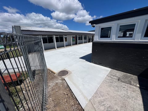 Modern rooftop terrace with metal fencing, white concrete surface, black industrial building, and blue sky with white clouds