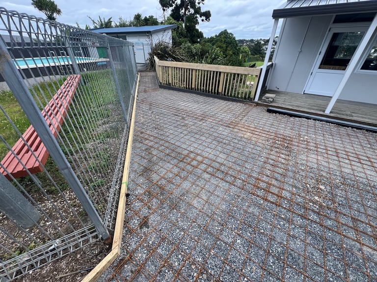 Paved outdoor area with metal fence on left, wooden railing in background, and small building with metal roof on right