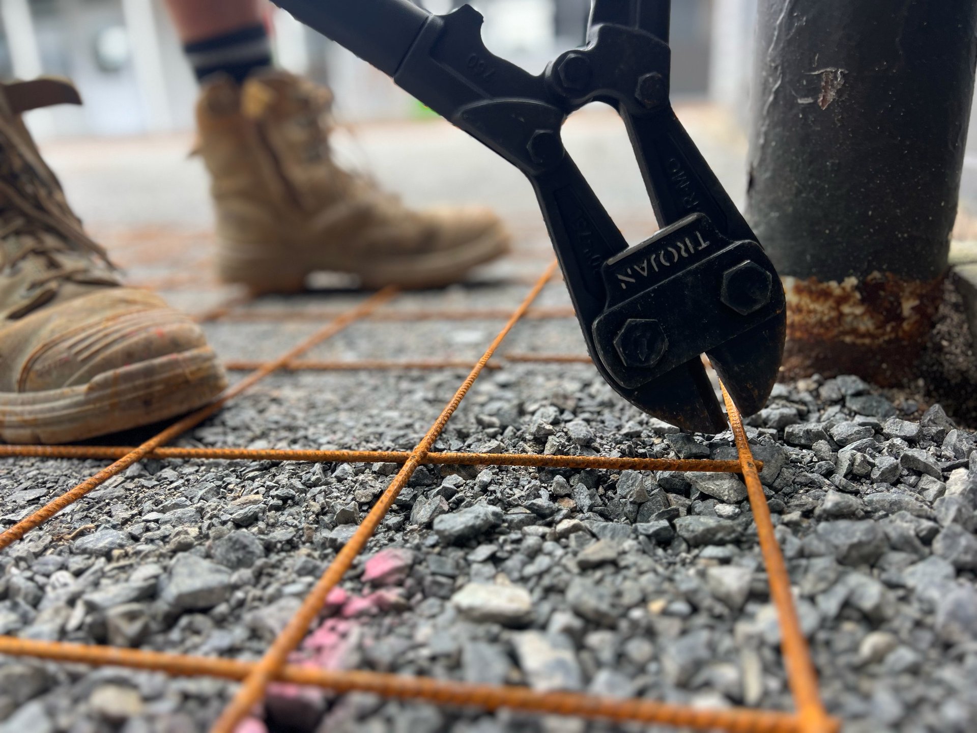 Close-up of hiking boot sole stepping on rocky ground near a tree with orange rope visible