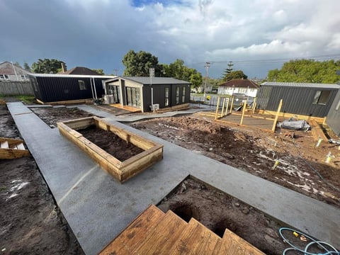 Modern sustainable homes under construction with raised garden beds, concrete foundation, and wooden decking on a residential property