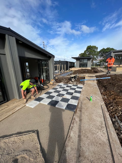 Construction worker in yellow vest installing black and white checkered floor tiles at a residential building site