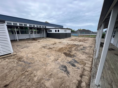Modern equestrian facility with sand arena, white-trimmed buildings, and fencing under cloudy sky