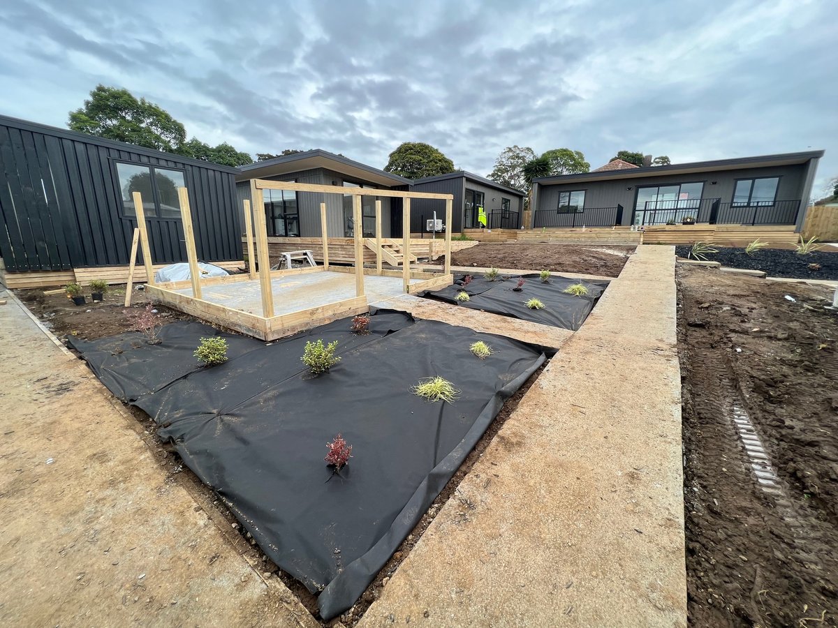 Construction site showing new modular homes under development with framed structures, landscaping fabric, and planted saplings in cleared outdoor areas