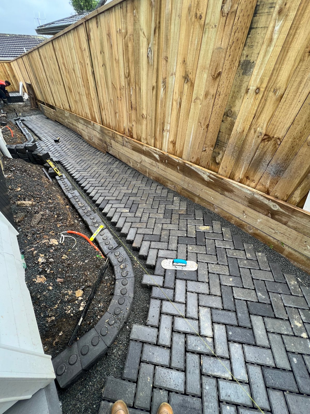 New paver walkway installation against wooden fence with landscape edging and construction tools visible