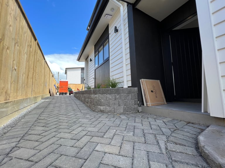 Modern house exterior with paved driveway, wooden fence, black garage door, and clear blue sky