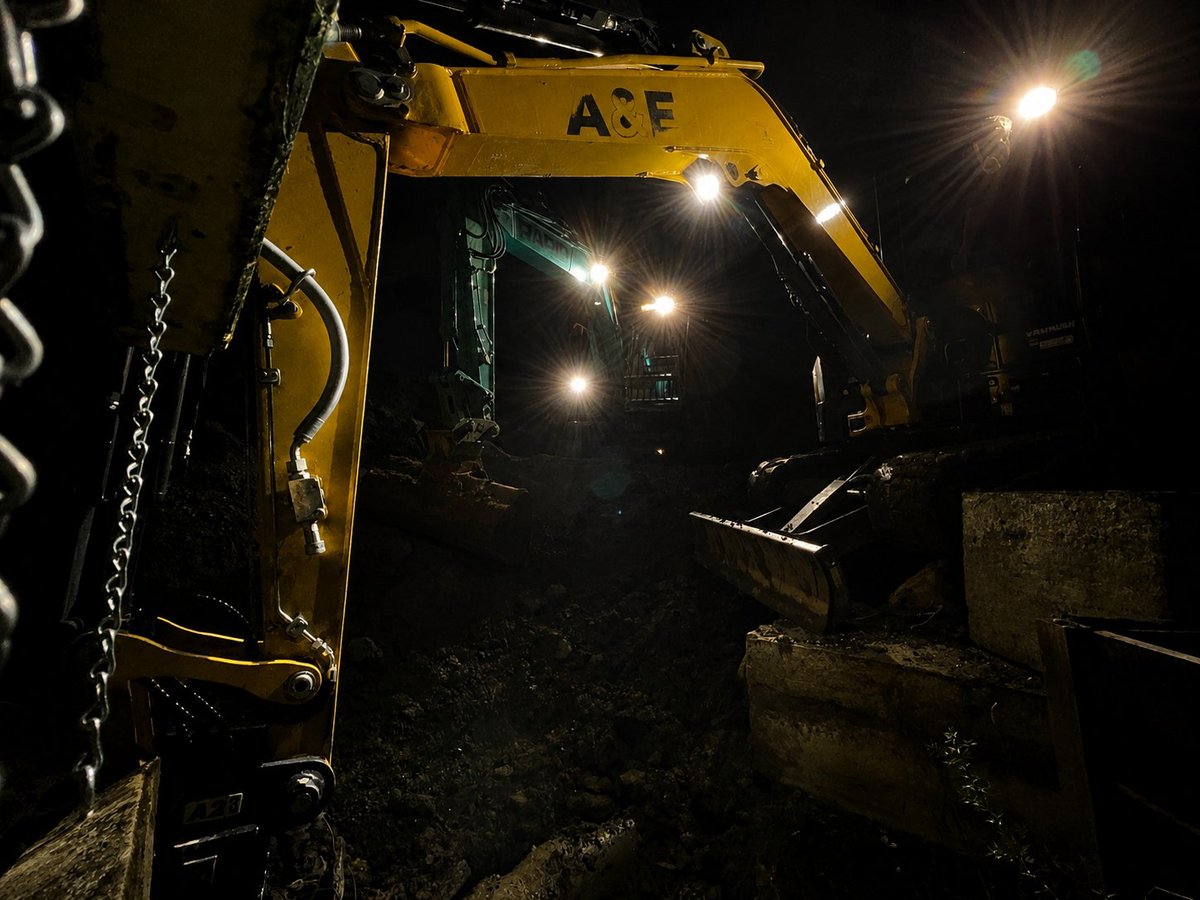 Yellow A&F excavator with LED lights operating at night in a dark construction site