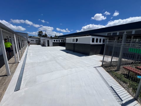 Industrial warehouse compound with white concrete courtyard, black metal-clad buildings, and clear blue sky with white clouds