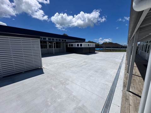 Rooftop industrial area with white concrete surface, metal buildings, clear blue sky with white clouds, and wooden railings