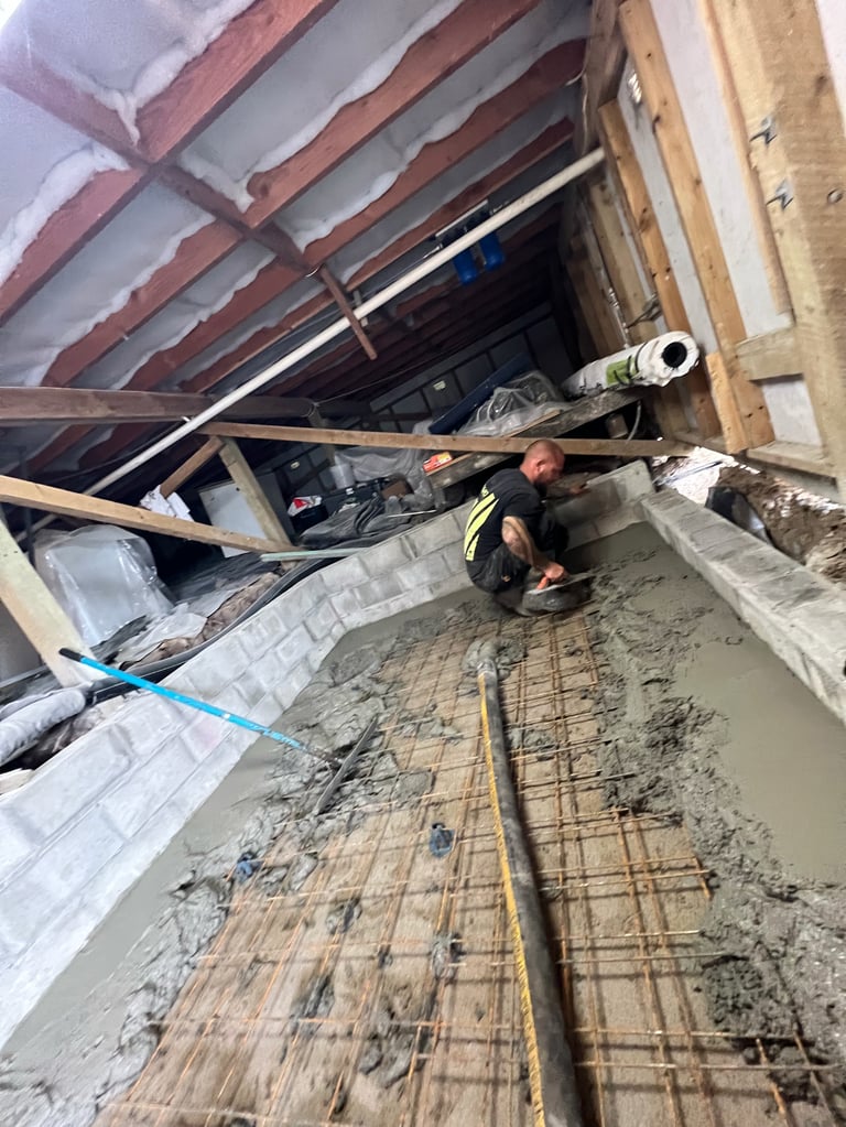 Construction worker in safety vest pouring concrete into foundation with steel rebar reinforcement visible