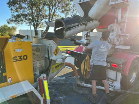 Worker operating a yellow Jacon S30 concrete pump during daytime outdoor construction work