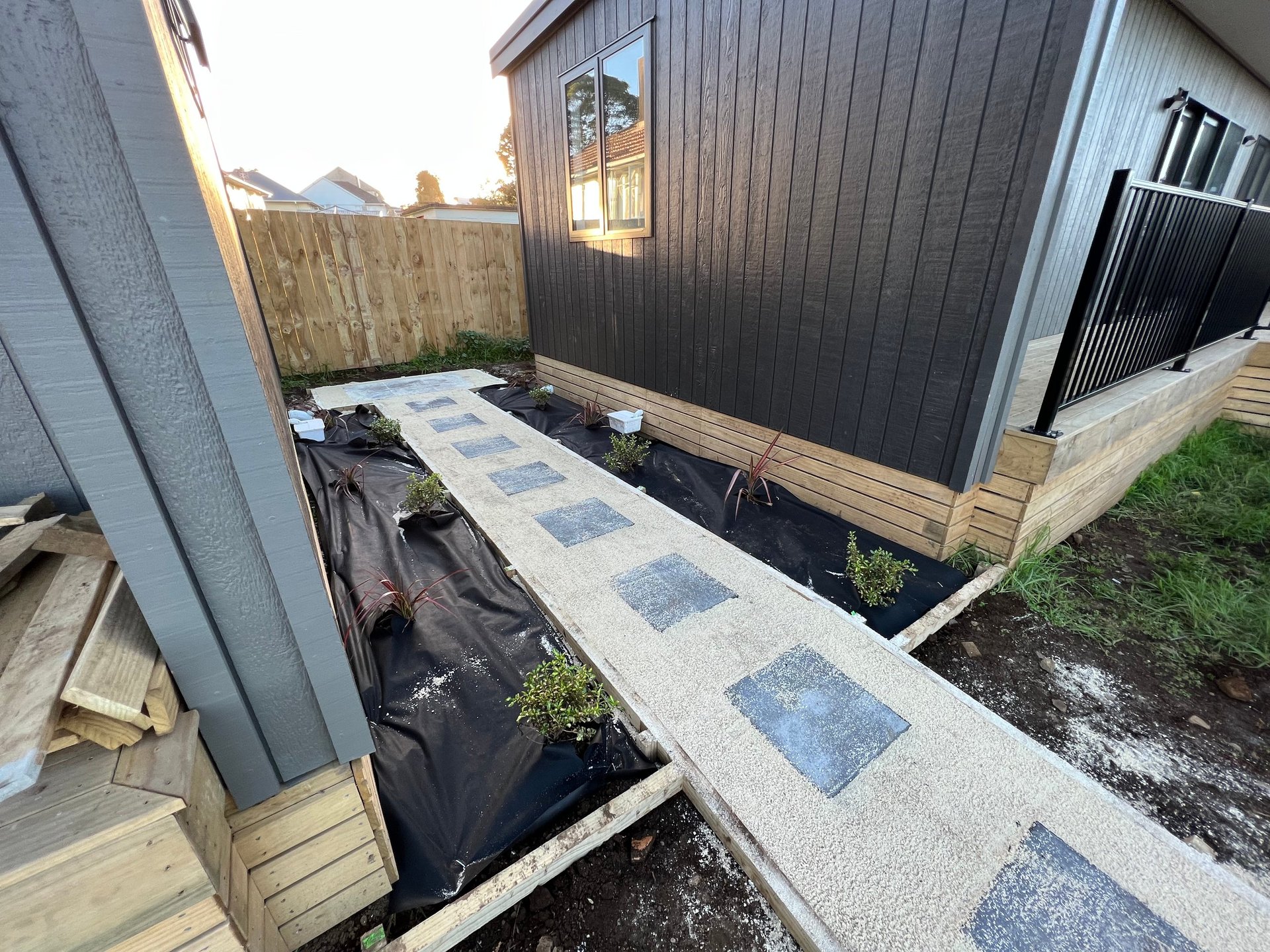 Narrow pathway with blue and gray paver stones between two residential buildings and dark fence